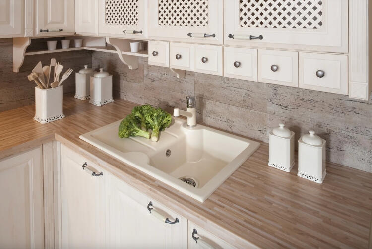 Detailný pohľad na umývadlo v rustikálnej kuchyni Decodom Katy s dekoratívnymi bielymi skrinkami a ratanovými dvierkami.